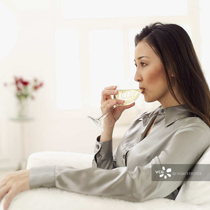 年轻女子侧身坐着喝白葡萄酒图片素材