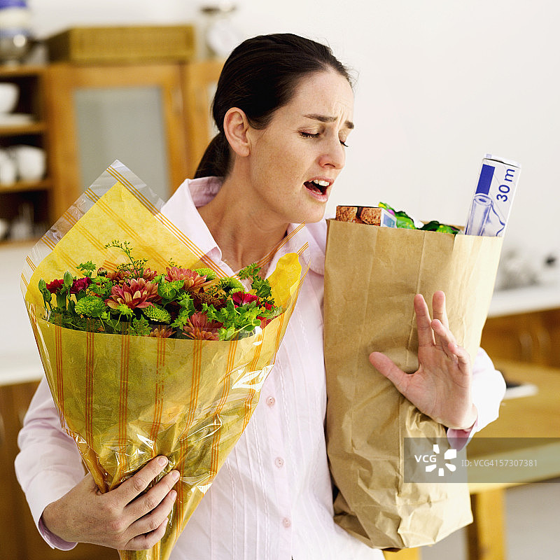 拿着装着食品杂货和鲜花的棕色纸袋的年轻女人图片素材
