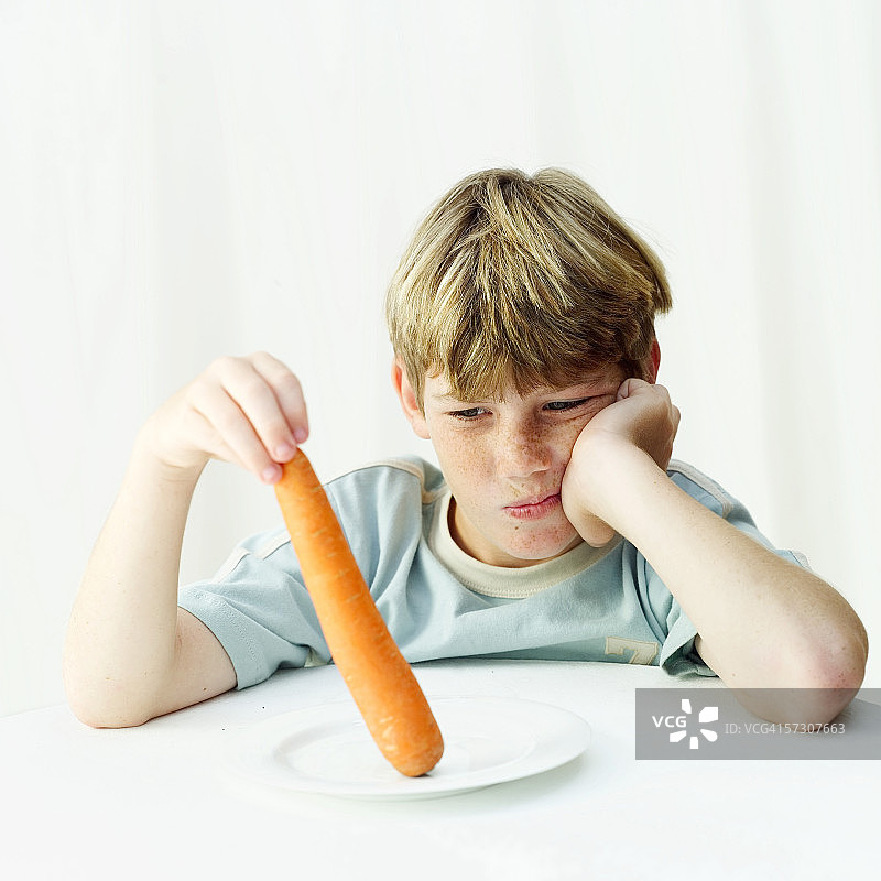 年轻男孩（12-14岁）看着手中的胡萝卜图片素材