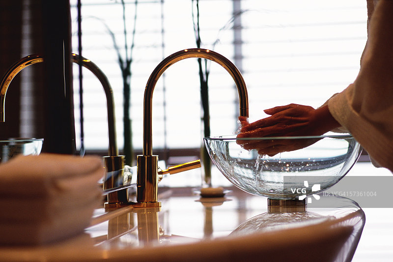 人在浴室洗手池边，水流过手指，背景是金茂大厦（君悦酒店）图片素材