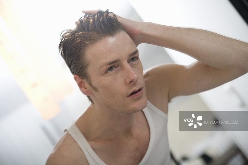 男人站在镜子前，手放在头发上图片素材