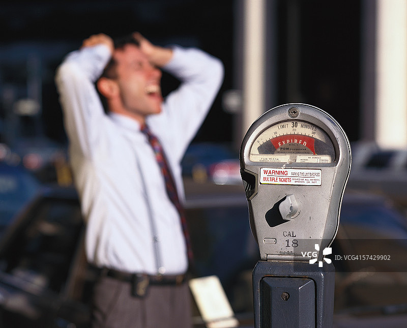 年轻商人站在过期停车计时器旁，双手抱头图片素材