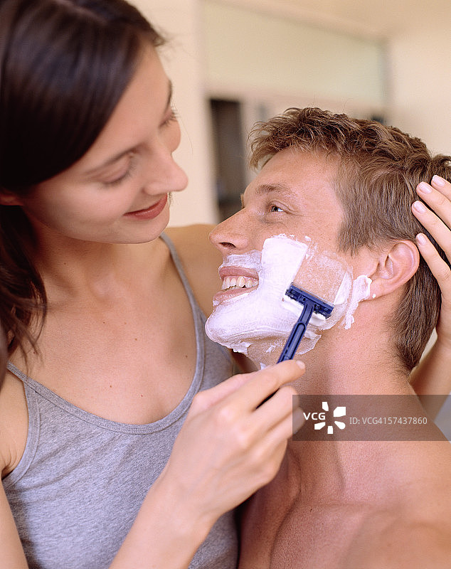 年轻女子用剃须刀为年轻男子刮胡子图片素材