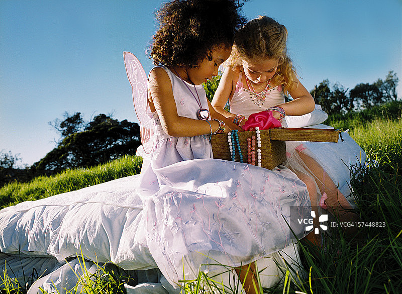 打扮成仙女坐在户外床上看盒子的两位小女孩图片素材