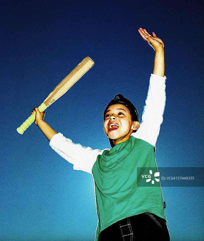 仰视：快乐男孩拿着棒球棒跳跃图片素材