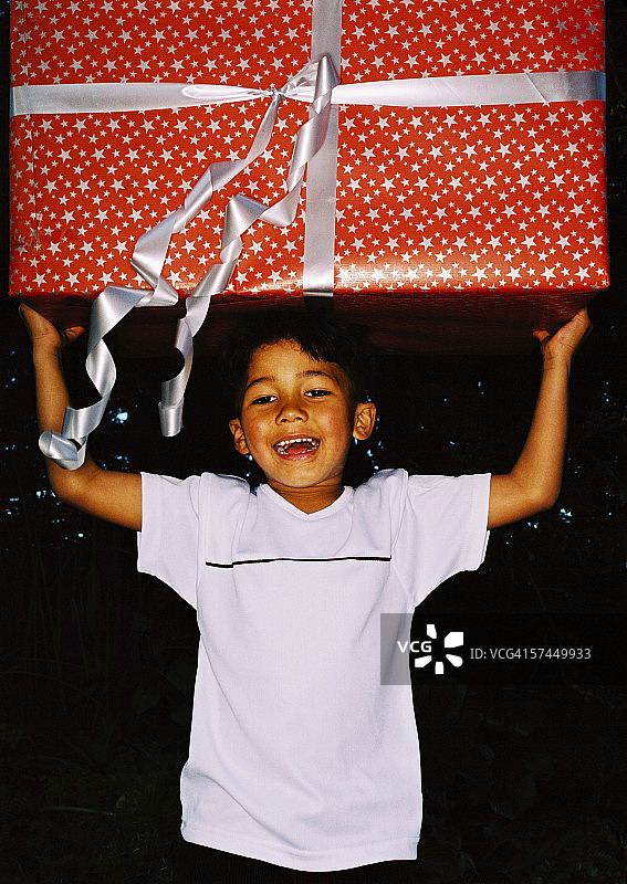 一个6-8岁的男孩头顶着巨大的生日礼物；微笑的肖像图片素材