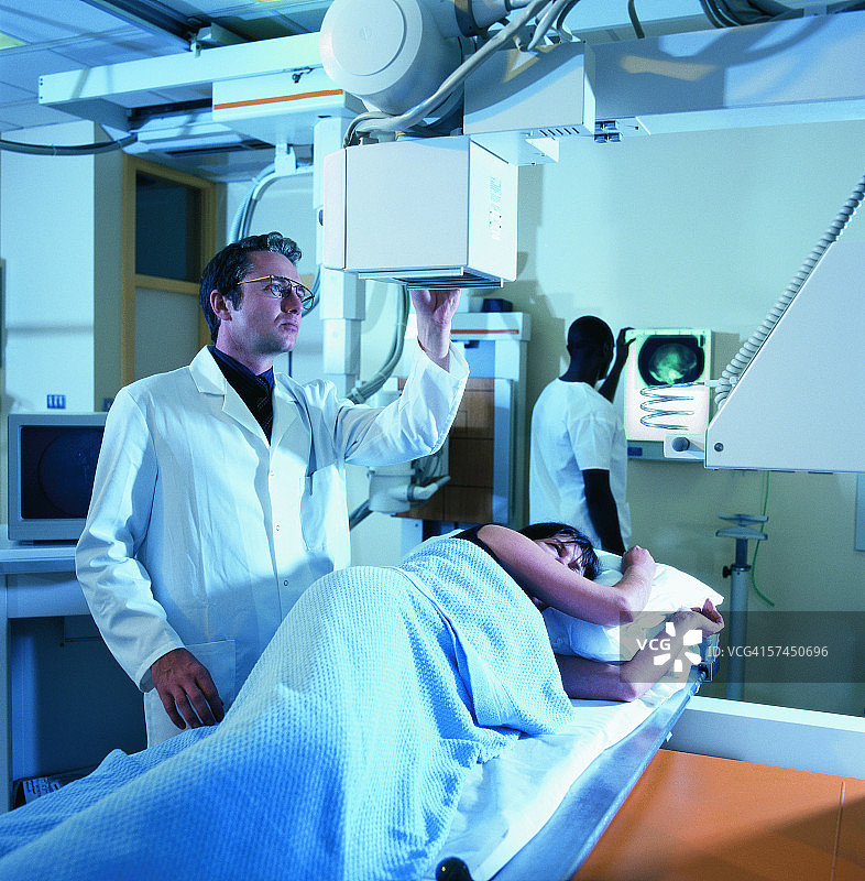 女病人躺在X光检查台上，男技师正在调整设备图片素材