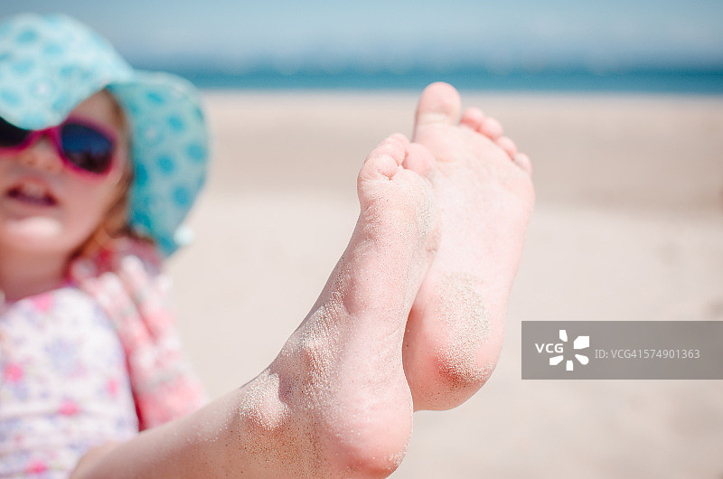 女孩在海滩上炫耀她沾满沙子的脚趾图片素材