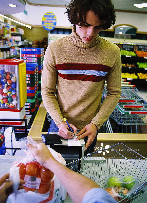 年轻男人在超市收银台签署信用卡收据图片素材