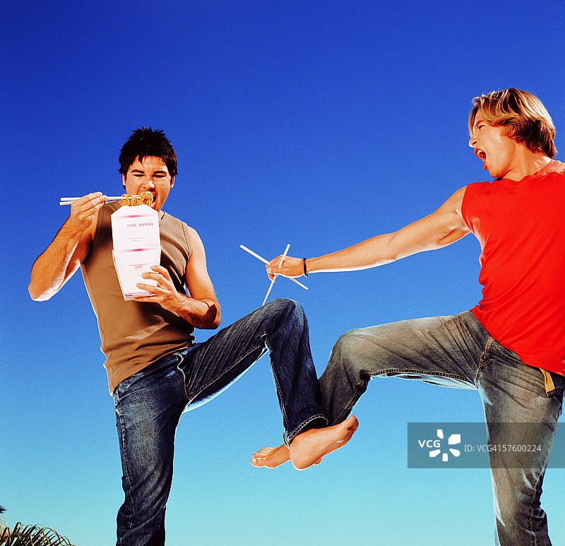 两个年轻男人吃中餐外卖时进行跆拳道训练的仰视角度图片素材