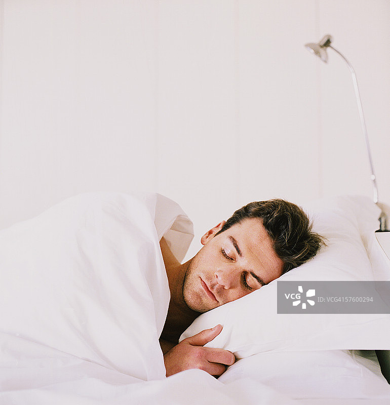年轻男子盖着被子在床上睡觉图片素材