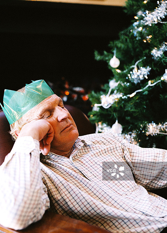 老年男人在圣诞树旁边的椅子上睡觉的低角度视图图片素材