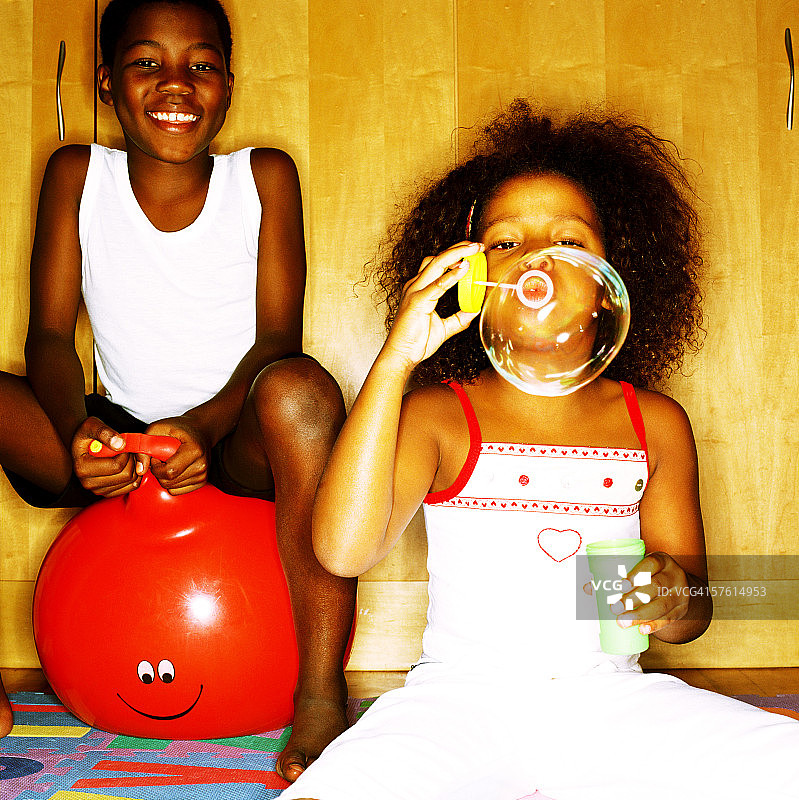年轻女孩吹肥皂泡，身后坐着弹跳球的男孩图片素材
