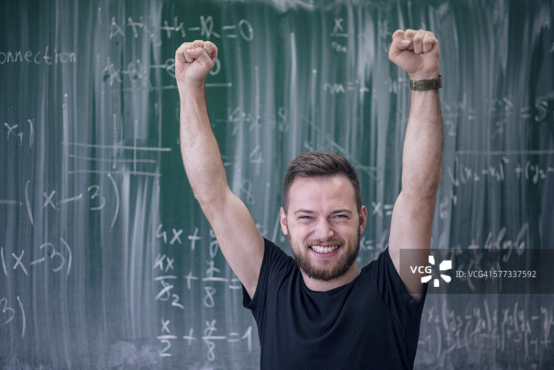 兴奋的微笑学生在黑板前举起双臂图片素材