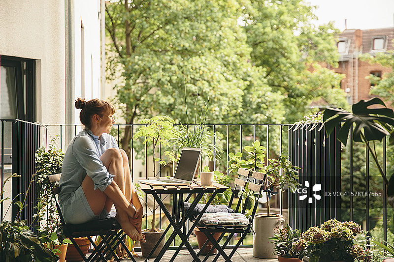 在阳台上看着笔记本电脑的微笑女人图片素材