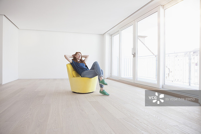 年轻女人坐在空荡荡的客厅里的黄色扶手椅上。图片素材