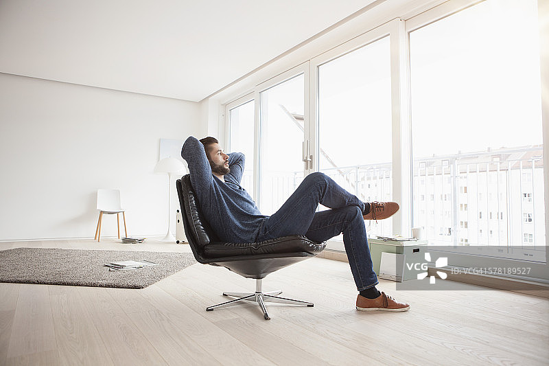 在他的客厅里坐在皮椅上放松的年轻男人图片素材