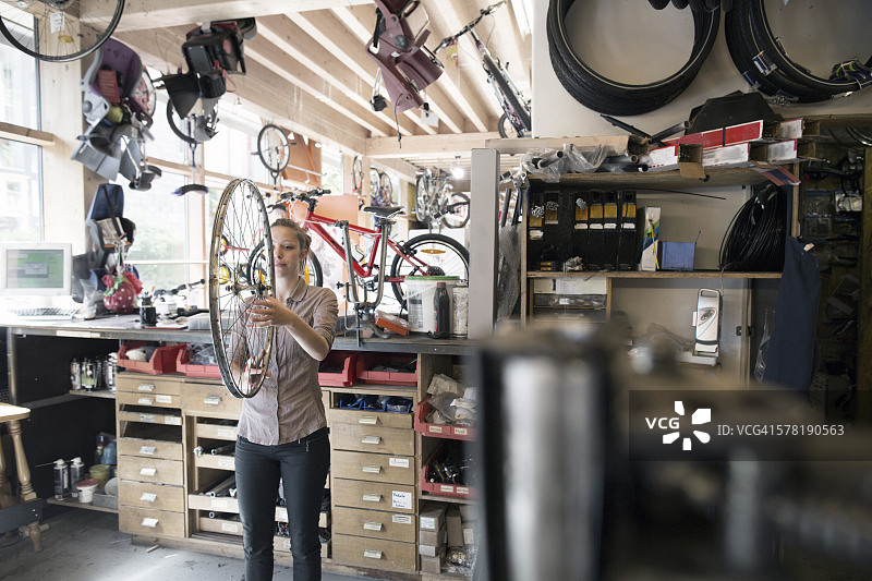 在修理店里拿着自行车轮的年轻女子图片素材