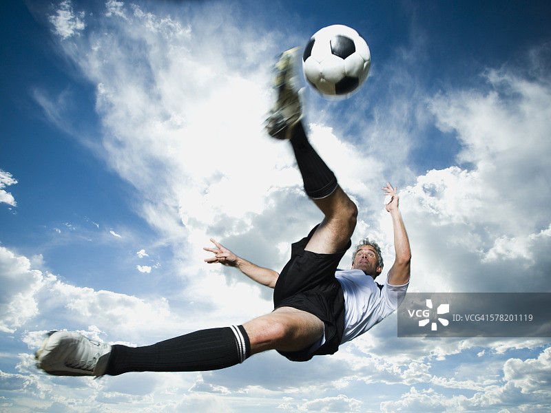 足球运动员在多云的蓝色天空下的剪影中踢球图片素材
