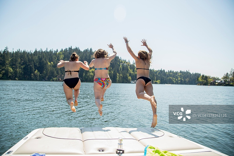 三名年轻女子从俄勒冈州奥斯威戈湖的码头跳下的背影，美国图片素材