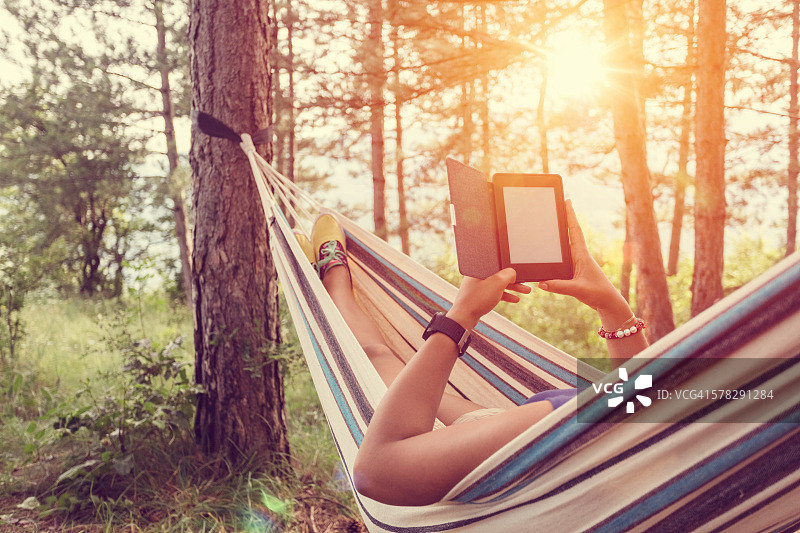 在吊床上看电子书的年轻女孩图片素材
