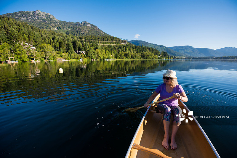 在原始湖上划独木舟的老年妇女图片素材