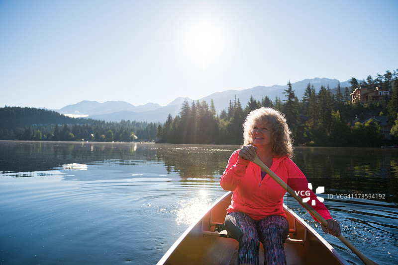 在原始湖上划独木舟的老年妇女图片素材