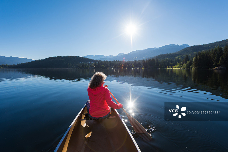 在原始湖上划独木舟的老年妇女图片素材