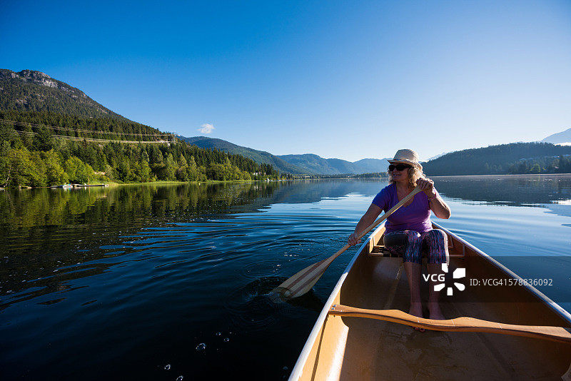在原始湖上划独木舟的老年妇女图片素材