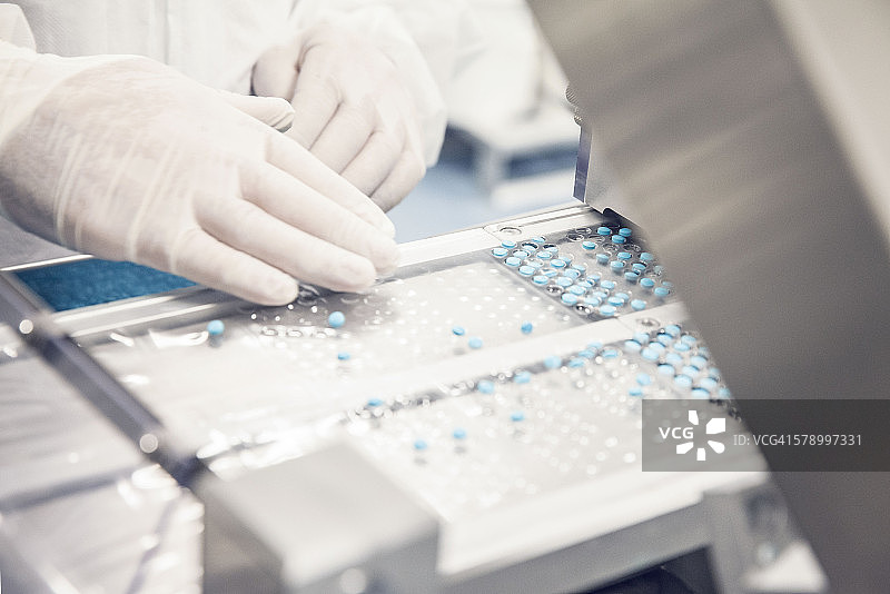 工人将药丸放入沿传送带移动的药片托盘中图片素材