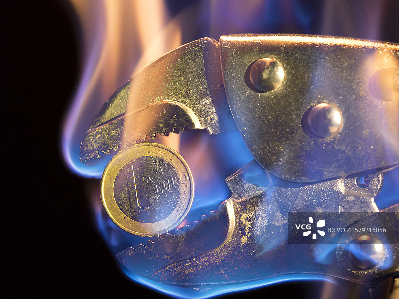 用钳子夹住放在火上的欧元硬币图片素材