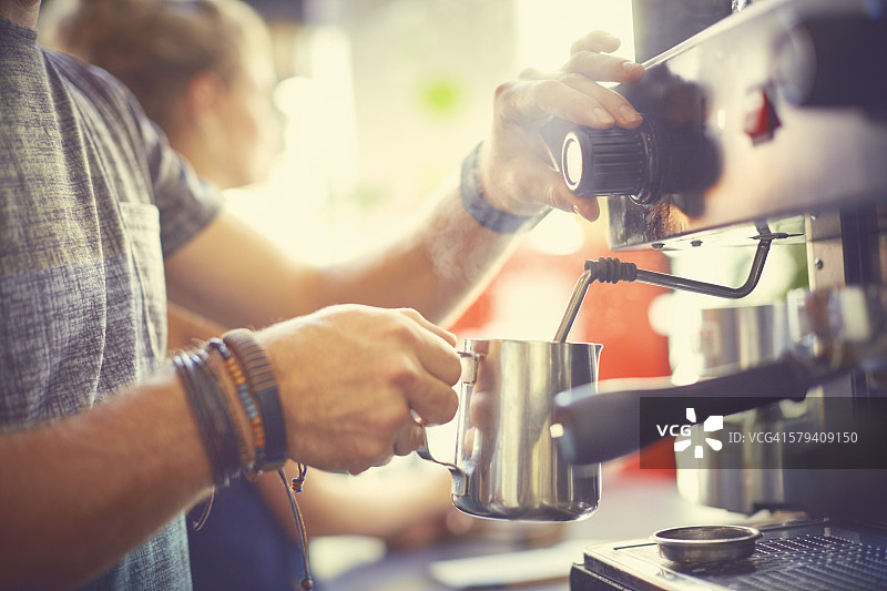 咖啡师在壶中蒸牛奶的腰部特写图片素材