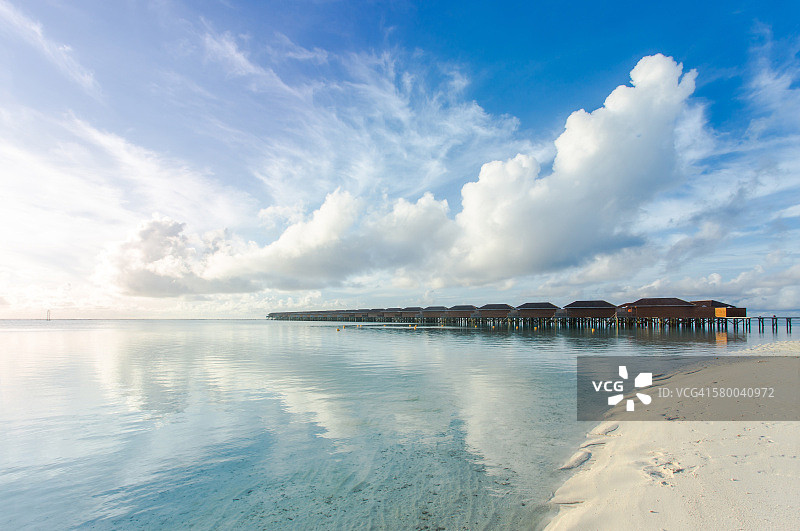 马尔代夫热带岛屿上的水上别墅（小屋），热带海滩上的白色沙滩和蓝色海水图片素材
