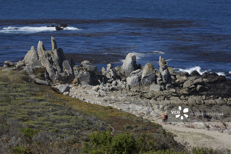 两人走在有岩石海岸线的沙滩上图片素材