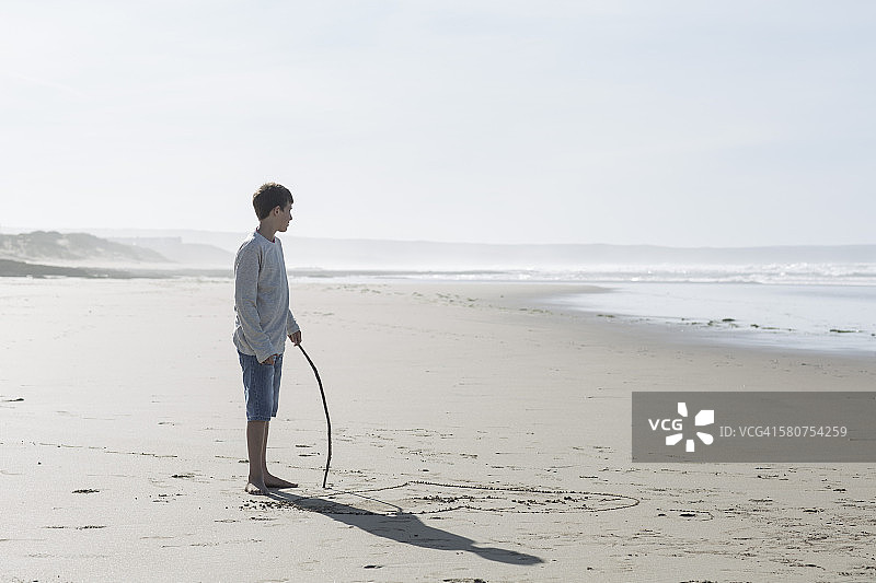 南非威士兰：站在海滩上拿着棍子的小男孩图片素材