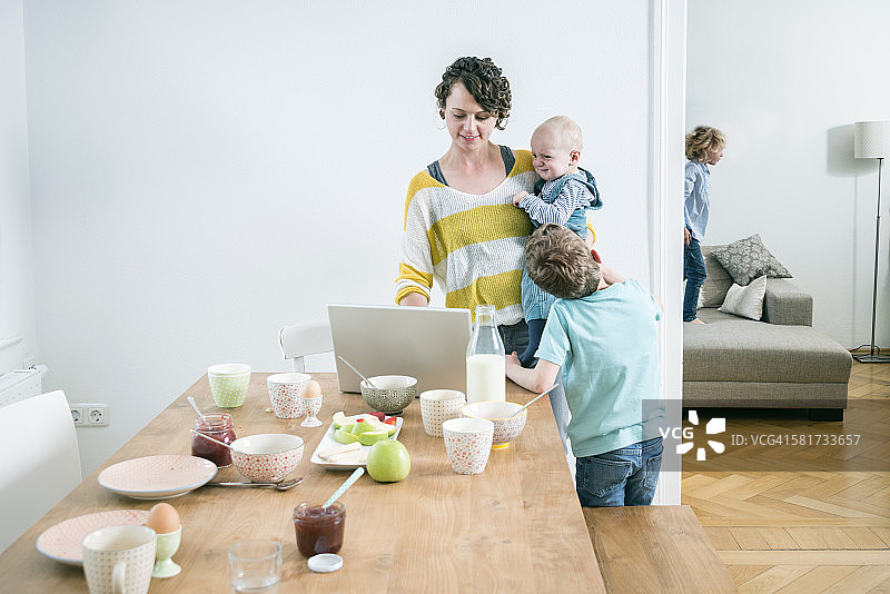 妈妈在厨房里用笔记本电脑和孩子们在一起图片素材