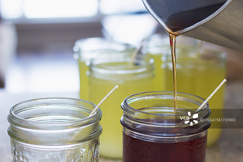 将热豆蜡倒入带有蜡烛灯芯的玻璃梅森罐中，制作自制礼品蜡烛的最后一步图片素材
