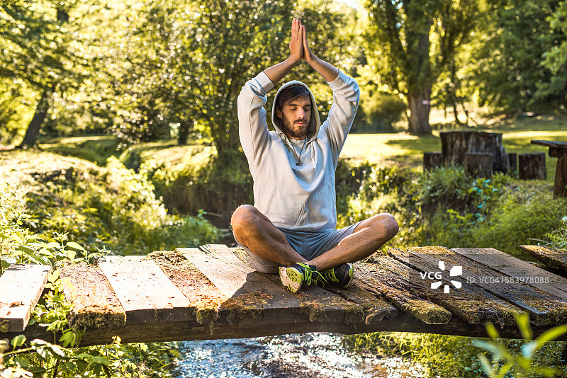 年轻男人在小溪上的桥上冥想图片素材