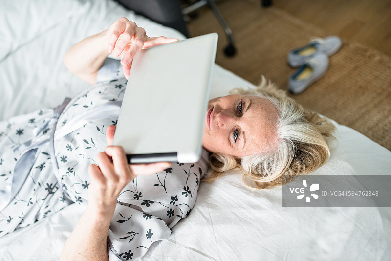 女人躺在床上使用平板电脑图片素材