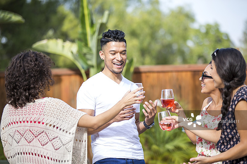年轻男子与成年姐妹在花园里分享玫瑰红葡萄酒祝酒图片素材