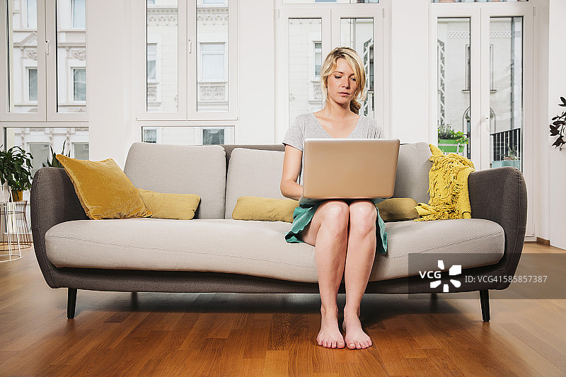 女人坐在客厅的沙发上使用笔记本电脑图片素材