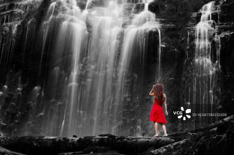 红裙赤脚女子站在瀑布下的背影，长曝光图片素材