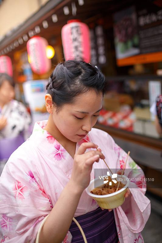 穿着浴衣的女人在节日街头品尝炖猪内脏图片素材