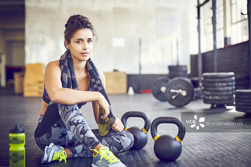 疲惫的女运动员坐在健身房的壶铃旁图片素材