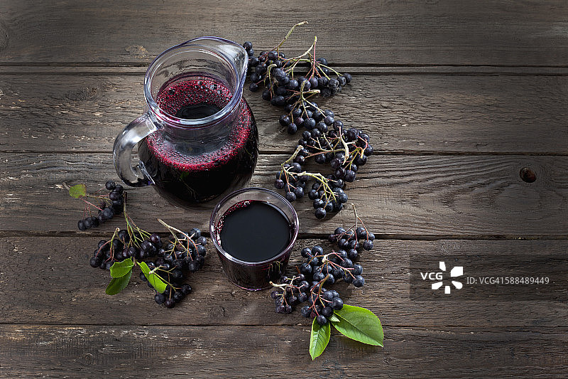 玻璃瓶、玻璃杯中的野樱莓汁和木头上的 chokeberry图片素材