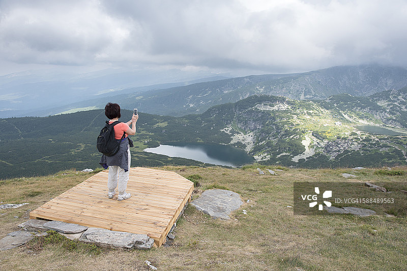 保加利亚里拉山脉老年妇女用智能手机拍照的背影图片素材