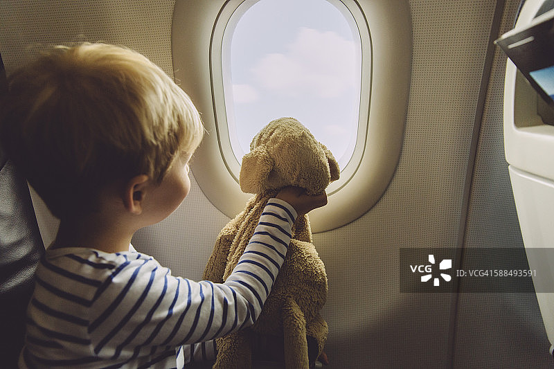 小男孩坐在飞机上，抱着玩具望向窗外图片素材