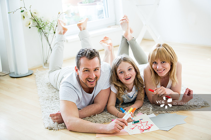 小女孩和父母躺在地板上用毡尖笔绘画图片素材