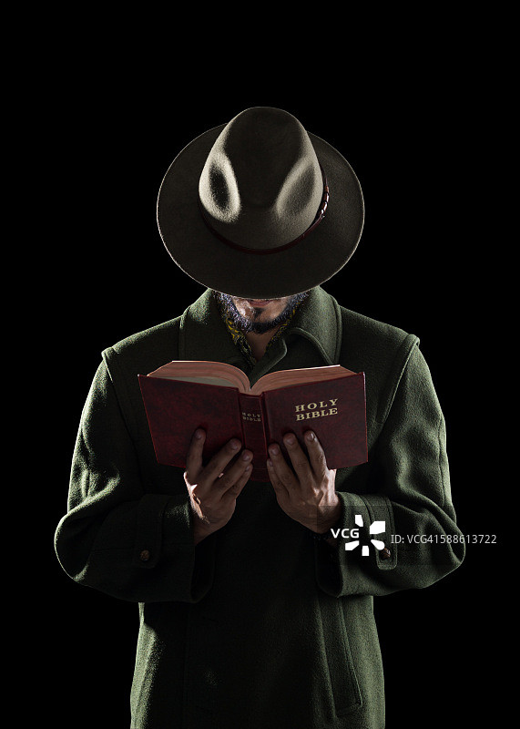 戴帽子的人在黑暗中阅读圣经图片素材