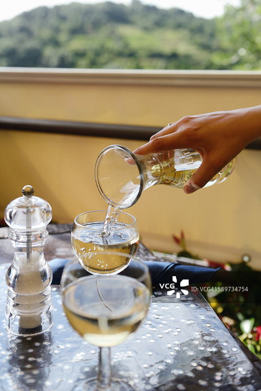 在餐厅露台的桌子上，手持玻璃瓶倒白葡萄酒图片素材